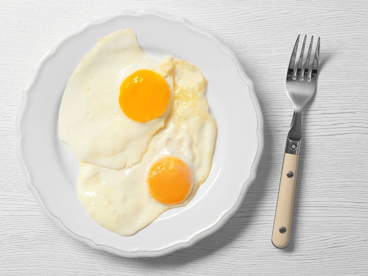 A plate with two over easy eggs next to a fork.