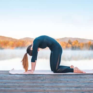 woman on wooden dock doing back strengthening exercise cat pose in front of lake